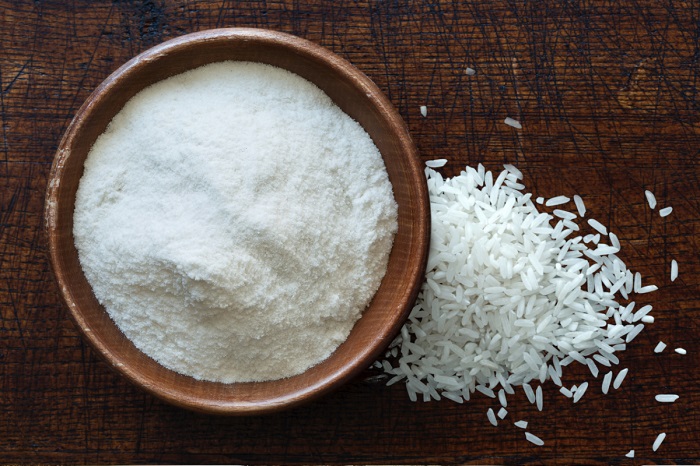 bowl of gluten free rice flour next to some rice grains on table 