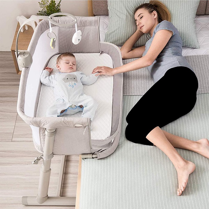 picture of new mom sleeping in a bed beside a baby in a co sleeper 