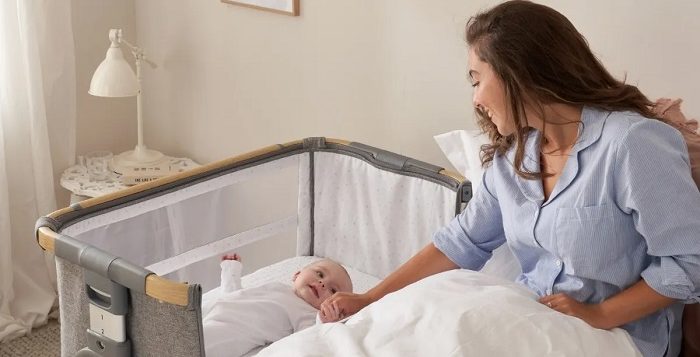 picture of a woman sitting in a bed beside a baby in a co sleepr crib