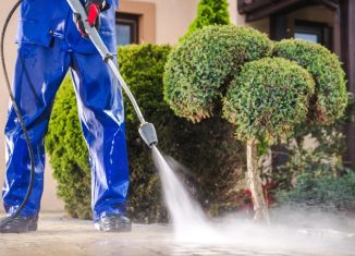 A guy dressed in blue power washing his driveway
